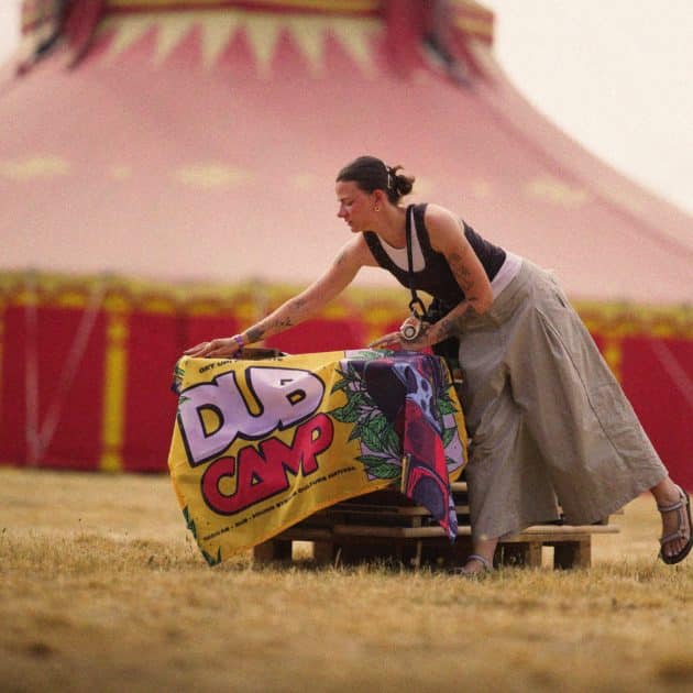 Femme posant le drapeau du Dub Camp 2026 sur une palette en bois devant un chapiteau du Dub Camp.