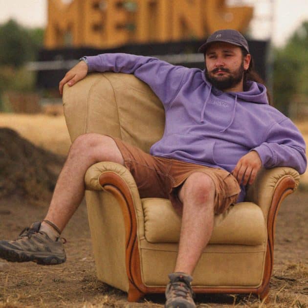 Homme posant sur un fauteuil crème avec le sweat-shirt violet du Dub Camp 2026