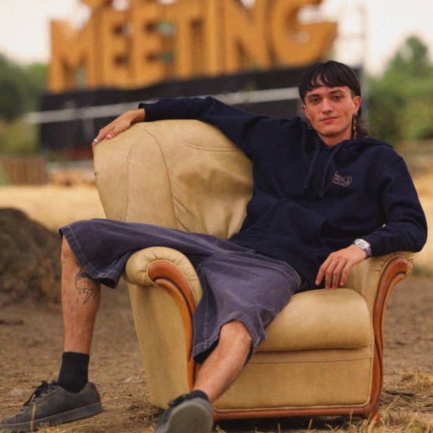 Homme posant sur un fauteuil crème, avec le sweat-shirt zappé bleu marine du Dub Camp 2026