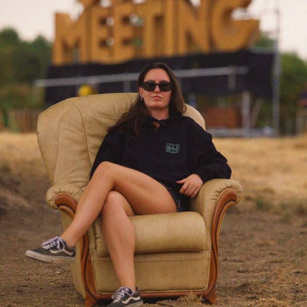 Femme posant sur un fauteuil crème, avec le sweat zippé noir du Dub Camp 2026