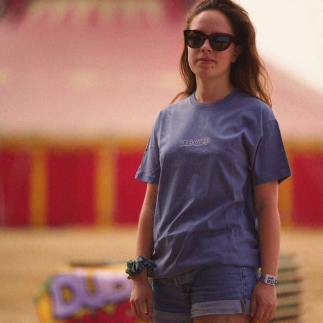 Femme posant devant un chapiteau du Dub Camp 2026, portant le T-shirt bleu de l'édition 2026