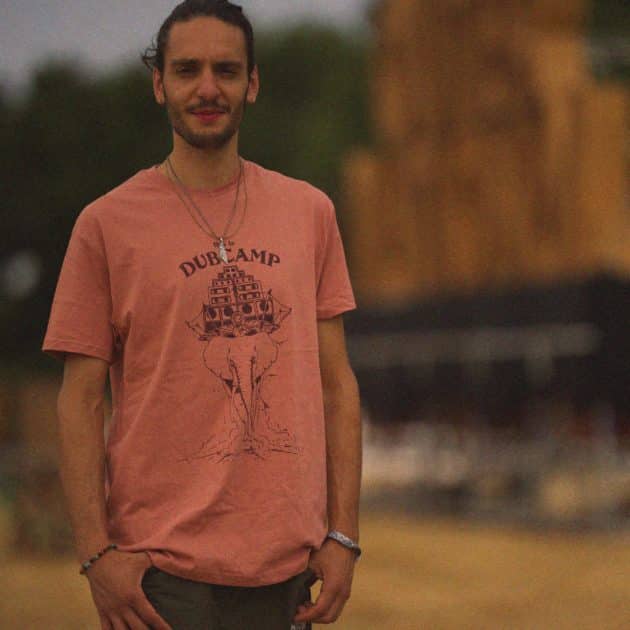 Homme posant avec un T-shirt rouge pâle Jata du Dub Camp 2026